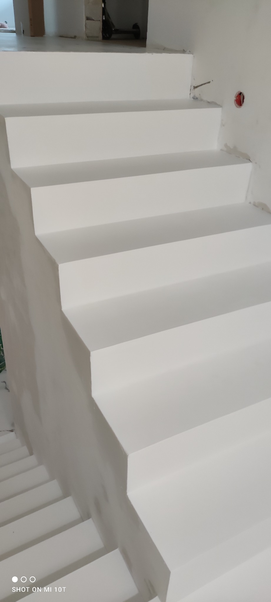 Betonowe schody wewnętrzne pomalowane na biało, widoczne ślady po szpachlowaniu na ścianie, gniazdko elektryczne w ścianie.