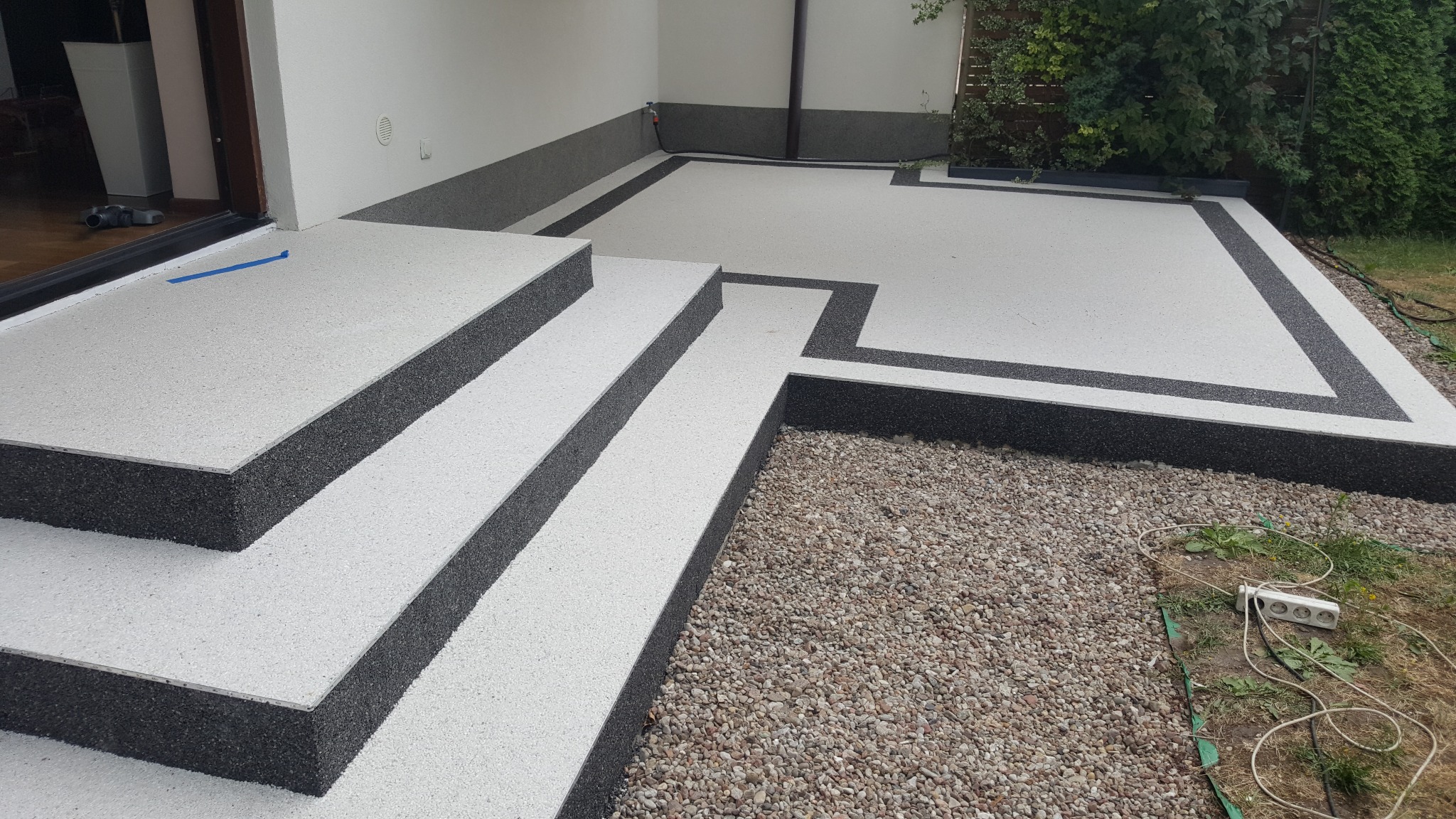 Wykończony taras z schodami z jasnej powierzchni z ciemnymi obramowaniami, widok z góry na zewnątrz budynku.