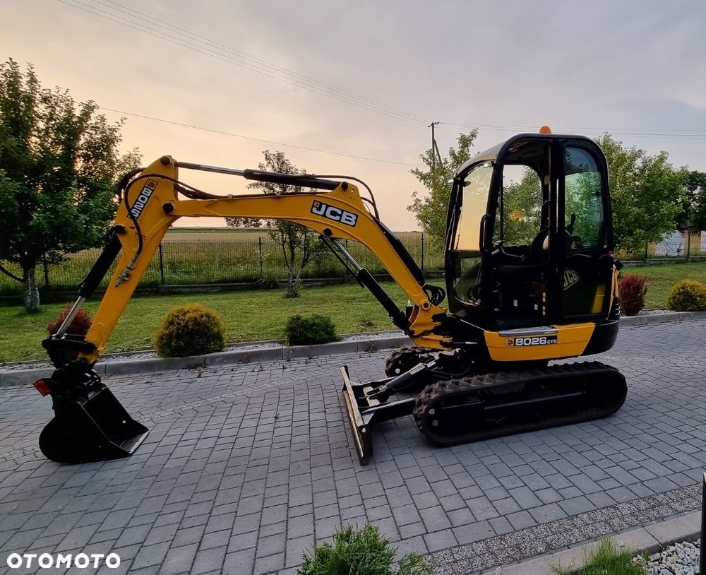 Żółto-czarna mini koparka JCB 8026 CTS na kostce brukowej, widok z boku, oświetlona popołudniowym słońcem.
