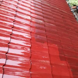 Częściowo umyta, czerwona blachodach&oacute;wka po prawej stronie pokryta zabrudzeniami i mchem, po lewej stronie czysta i lśniąca od wody.