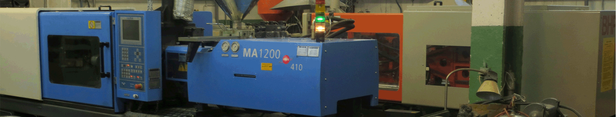 Niebieska wtryskarka MA1200 z panelami sterowania, sygnalizacją świetlną i pomarańczowym podajnikiem tworzywa sztucznego w hali produkcyjnej.