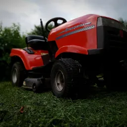 Czerwona kosiarka samojezdna Husqvarna na trawniku z widocznymi śladami świeżo skoszonej trawy, pochmurne tło z zielenią.