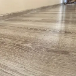 Jasne panele podłogowe z delikatnym wzorem drewna, świeżo położone w mieszkaniu w Łodzi, widoczne z niskiej perspektywy, z listwą przypodłogową w tle.