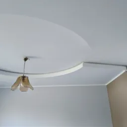 Pomalowany sufit z dekoracyjnym okręgiem i lampą w stylu retro, fragment ściany z imitacją cegły w rogu pomieszczenia.