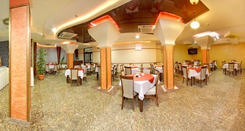 Przestronna sala restauracyjna w hotelu z kolumnami, stołami nakrytymi białymi obrusami i czerwonymi serwetami, oraz marmurową podłogą.