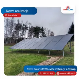 Instalacja paneli fotowoltaicznych Swiss Solar 445Wp o mocy 9.79kWp na zielonej działce w Czarnówku, widok z niskiej perspektywy, w tle drzewa i pochmurne niebo.