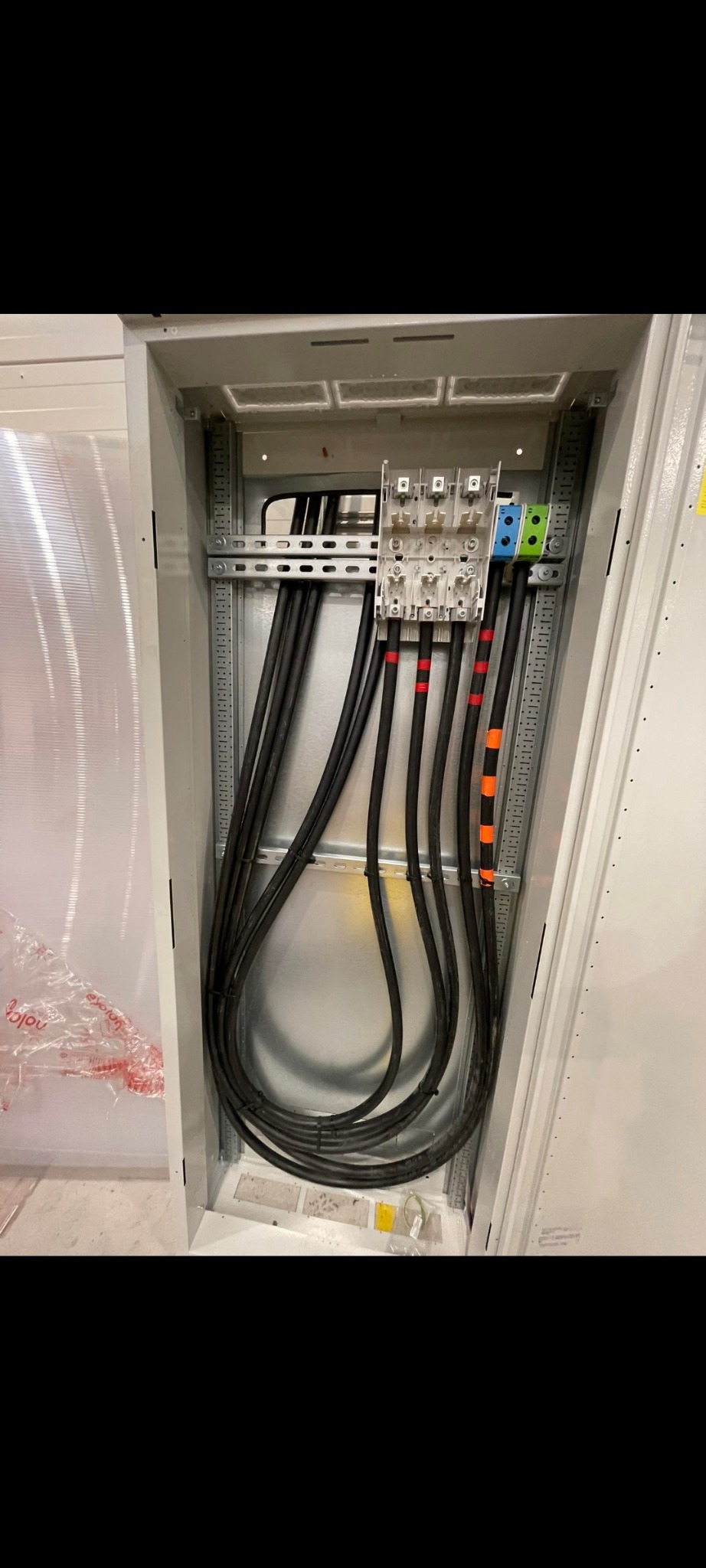 Rozdzielnia elektryczna wewnątrz metalowej szafy z czarnymi kablami oznaczonymi kolorowymi paskami, podłączonymi do listwy zaciskowej. Widoczne elementy montażowe.