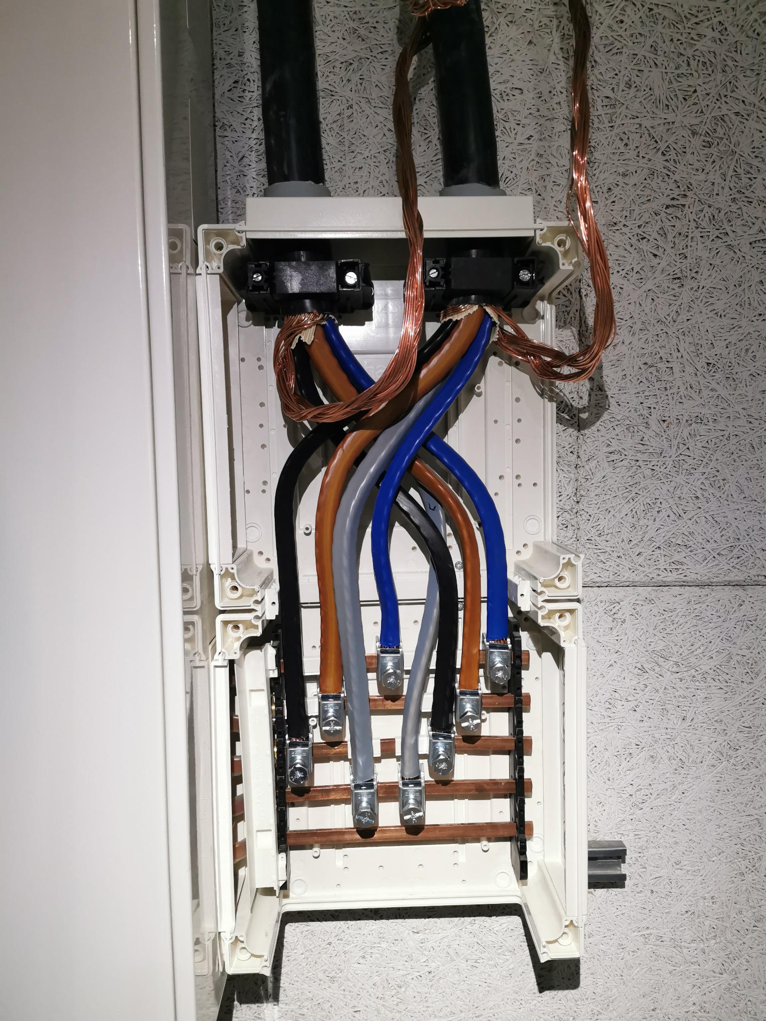 Otwarta skrzynka elektryczna z kolorowymi kablami i przewodami miedzianymi na ścianie. Widoczne złącza i elementy instalacyjne. Detal instalacji wewnątrz obiektu.