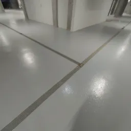 Jasnoszara, błyszcząca posadzka w garażu podziemnym z widocznymi brązowymi listwami dylatacyjnymi układającymi się w geometryczny wz&oacute;r.