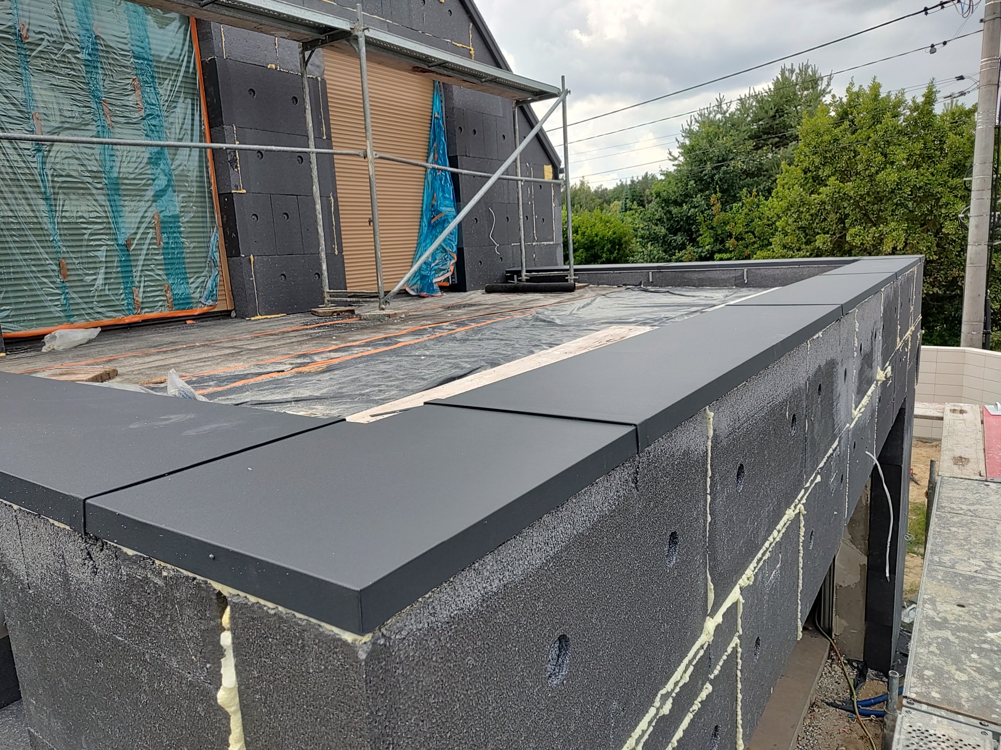 Ocieplenie budynku styropianem grafitowym z wykończeniem, widoczne rusztowanie i zabezpieczenia. Detal na łączeniu płyt izolacyjnych.