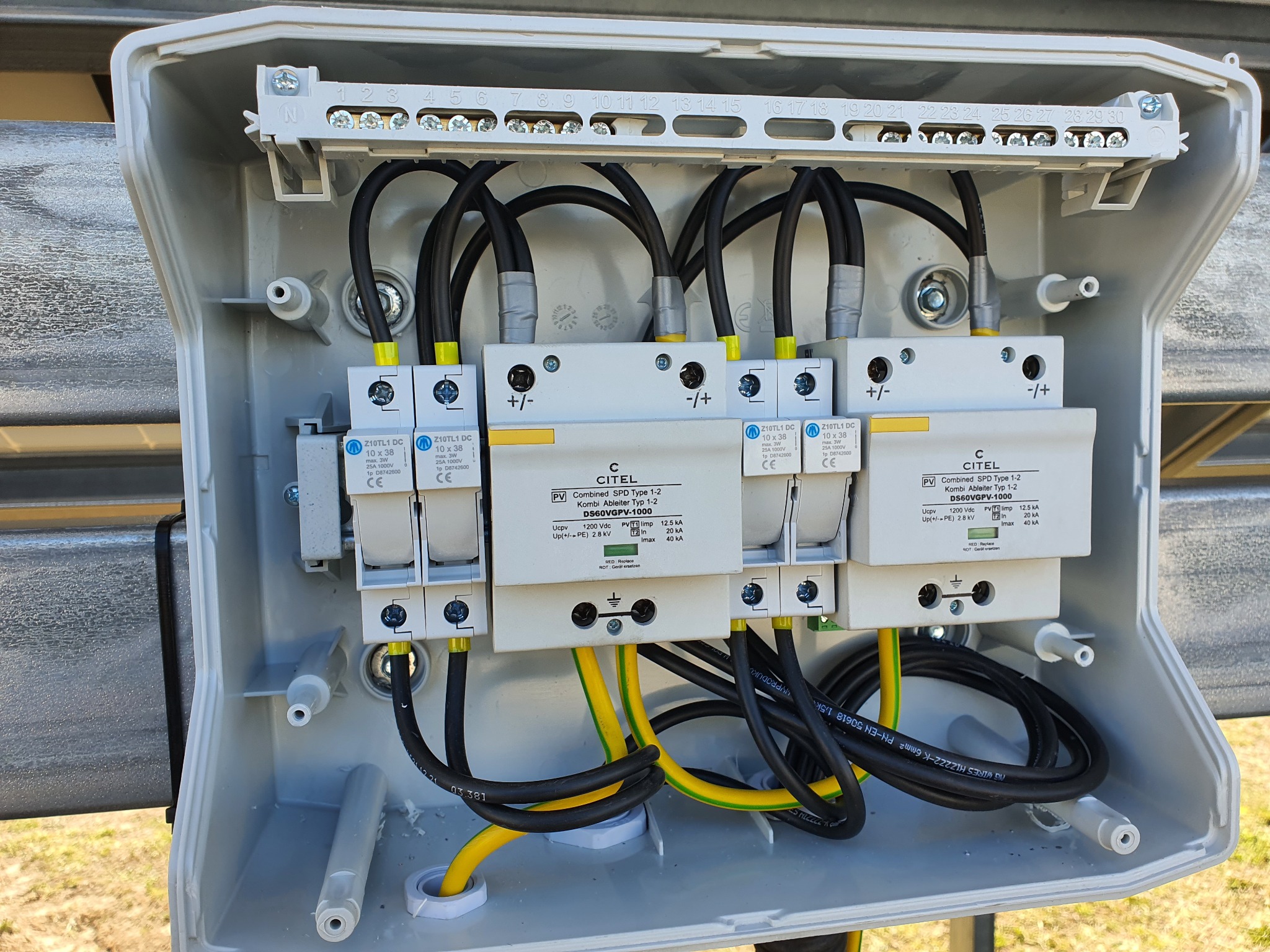 Rozdzielnica fotowoltaiczna z zabezpieczeniami przepięciowymi CITEL DS60VGPV-1000, widoczne przewody czarne i żółto-zielone, listwa zaciskowa z numerowanymi polami w górnej części obudowy.
