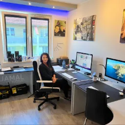 Kobieta siedząca przy biurku w nowoczesnym biurze z dwoma komputerami iMac, narzędziami Wera i Stanley, drukarką HP, zdjęciami na ścianach i oświetleniem LED.