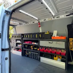 Wnętrze furgonetki serwisowej z profesjonalnym systemem regałów i pojemników na narzędzia, widoczny sprzęt marki DeWalt, gaśnica oraz logo firmy Jamal Budujemy Wasze Marzenia.