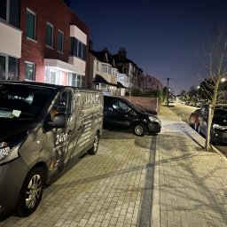 JAMAL Sp. z o.o. - Szary samochód dostawczy z logo firmy Jamal Expert Home Services zaparkowany na chodniku w nocy, z widocznymi numerami telefonów i informacją o 24-godzinnym pogotowiu elektrycznym i hydraulicznym...