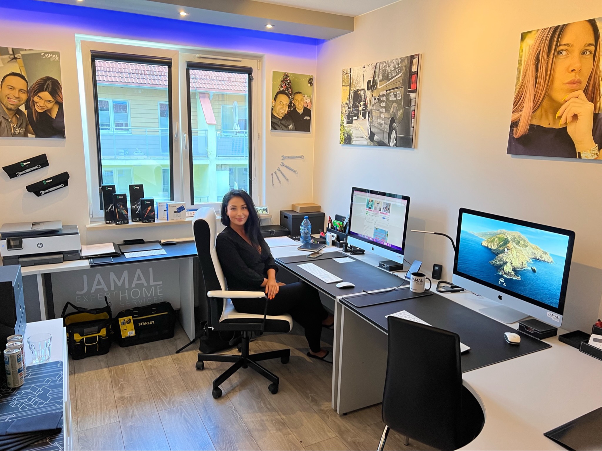 Kobieta siedząca przy biurku w nowoczesnym biurze z dwoma komputerami iMac, narzędziami Wera i Stanley, drukarką HP, zdjęciami na ścianach i oświetleniem LED.