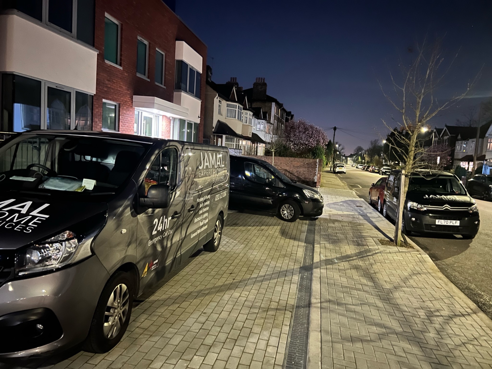 Szary samochód dostawczy z logo firmy Jamal Expert Home Services zaparkowany na chodniku w nocy, z widocznymi numerami telefonów i informacją o 24-godzinnym pogotowiu elektrycznym i hydraulicznym...