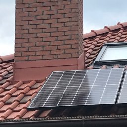 PlUAroof.pl - Czerwona dachówka ceramiczna z kominem z cegły, oknem dachowym i panelami słonecznymi w pochmurny dzień.