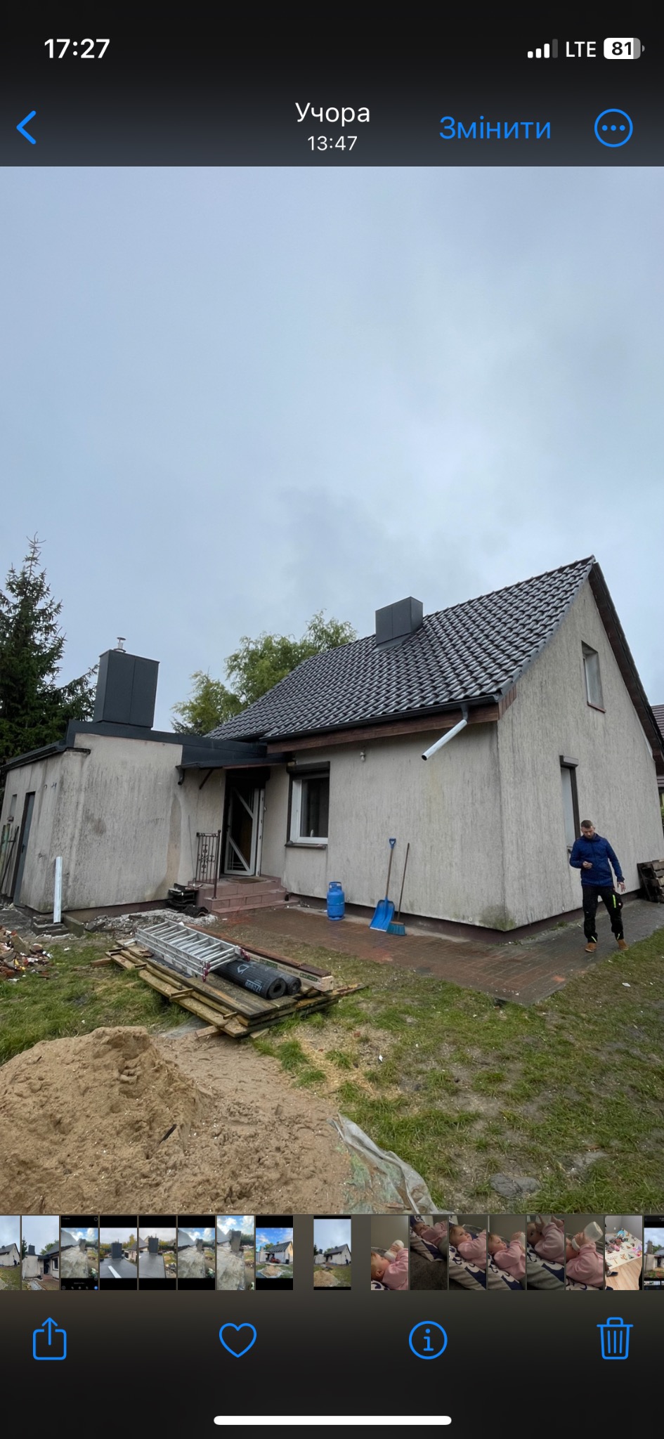 Dom jednorodzinny z nowym, ciemnym pokryciem dachowym, widoczne rynny, komin obłożony blachą, na ziemi leżą materiały budowlane i narzędzia, w tle pochmurne niebo.