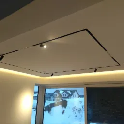 Nowoczesne oświetlenie sufitowe z czarnymi szynami i punktowymi reflektorami w białym wnętrzu, widok na zaśnieżony krajobraz za oknem.