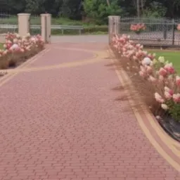 Kaskadowa ścieżka z czerwonej kostki, obramowana rabatami z hortensjami 'Limelight' i ozdobnymi trawami, oświetlona kulistymi lampami, w tle zielony trawnik i ozdobne ogrodzenie.