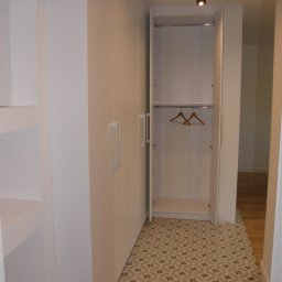 FRIZAR Meble Ryszard Kuchciński - Wnętrze przedpokoju z białą zabudową szafy wnękowej, otwarte drzwi ukazują dwie puste drewniane wieszaki na metalowym drążku, wzorzysta podłoga.