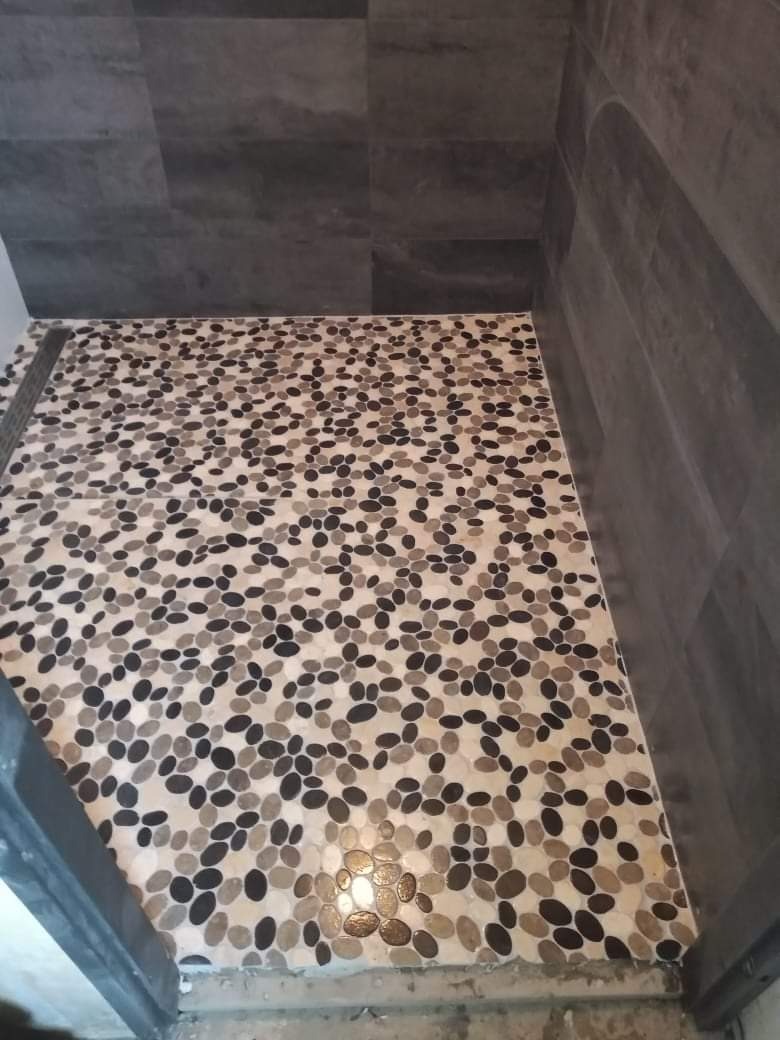 Wykończony fragment kabiny prysznicowej z mozaiką z kamyków na podłodze i szarą, imitującą kamień, okładziną ścienną.