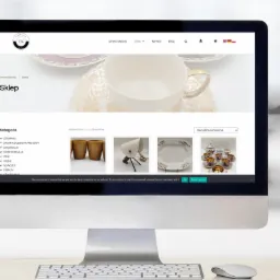 Ekran komputera iMac prezentuje stronę internetową sklepu z ceramiką Tajemniczy-Kredens.pl, z widocznymi kategoriami produktów i miniaturami naczyń.