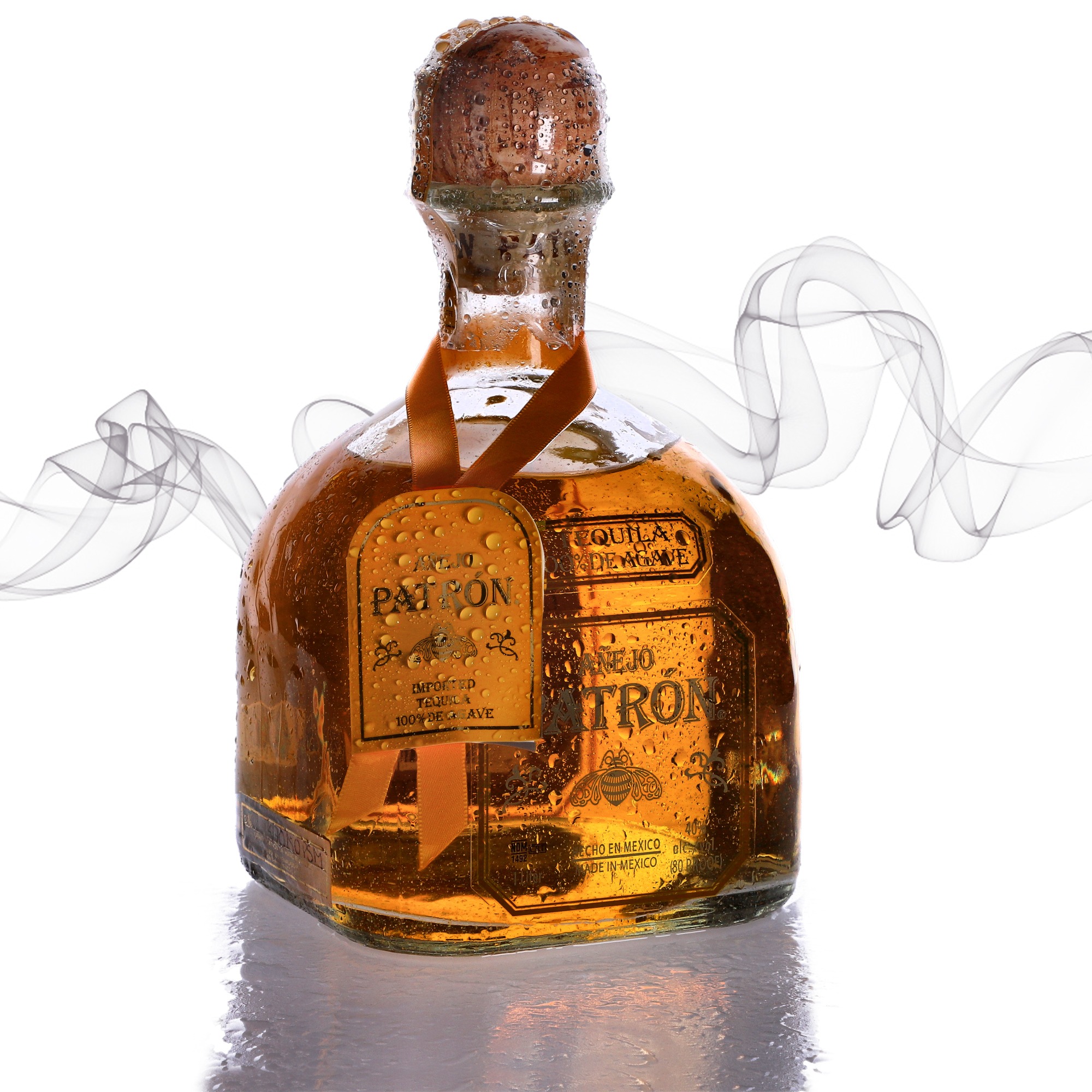 Butelka złotej tequili Patron Anejo z kroplami wody na etykiecie i korku, otoczona smugami dymu na białym tle.