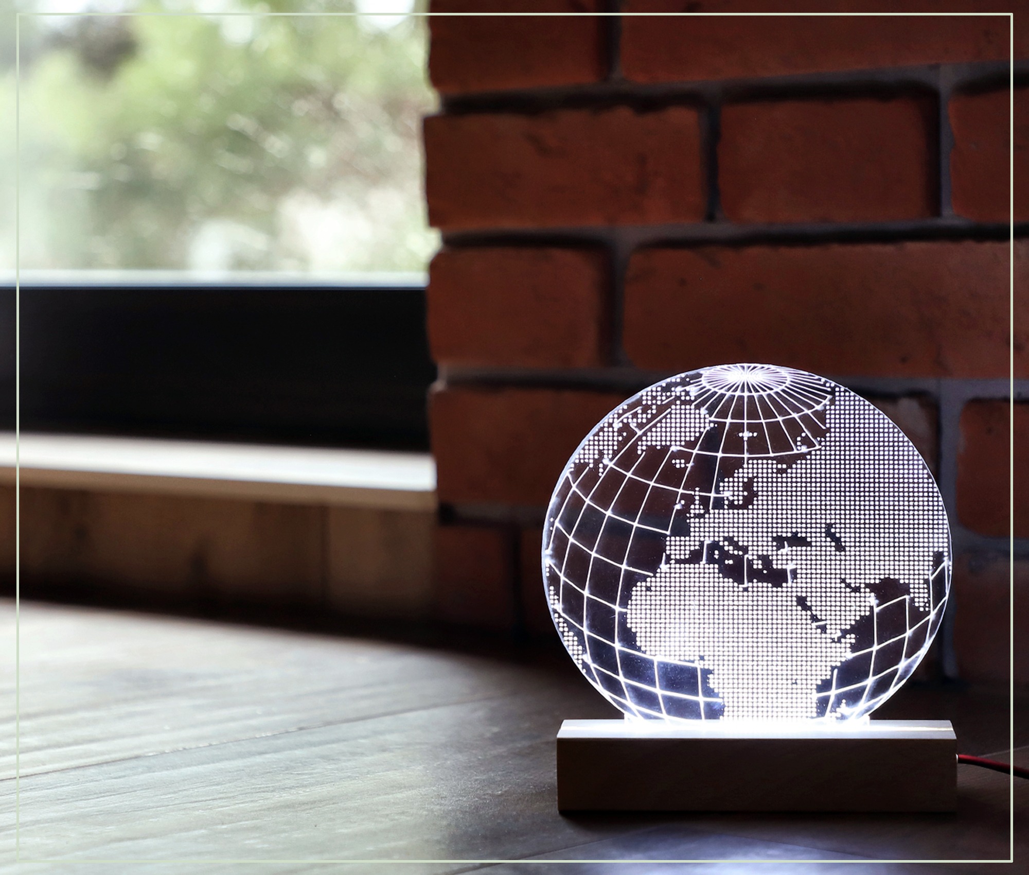 Podświetlany globus LED z zaznaczonymi kontynentami, stojący na drewnianej podstawie, na tle ceglanej ściany i okna.