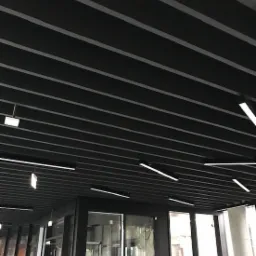 Czarny sufit rastrowy z liniowym oświetleniem LED w nowoczesnym biurze, widok z dołu na szklane drzwi i okna.