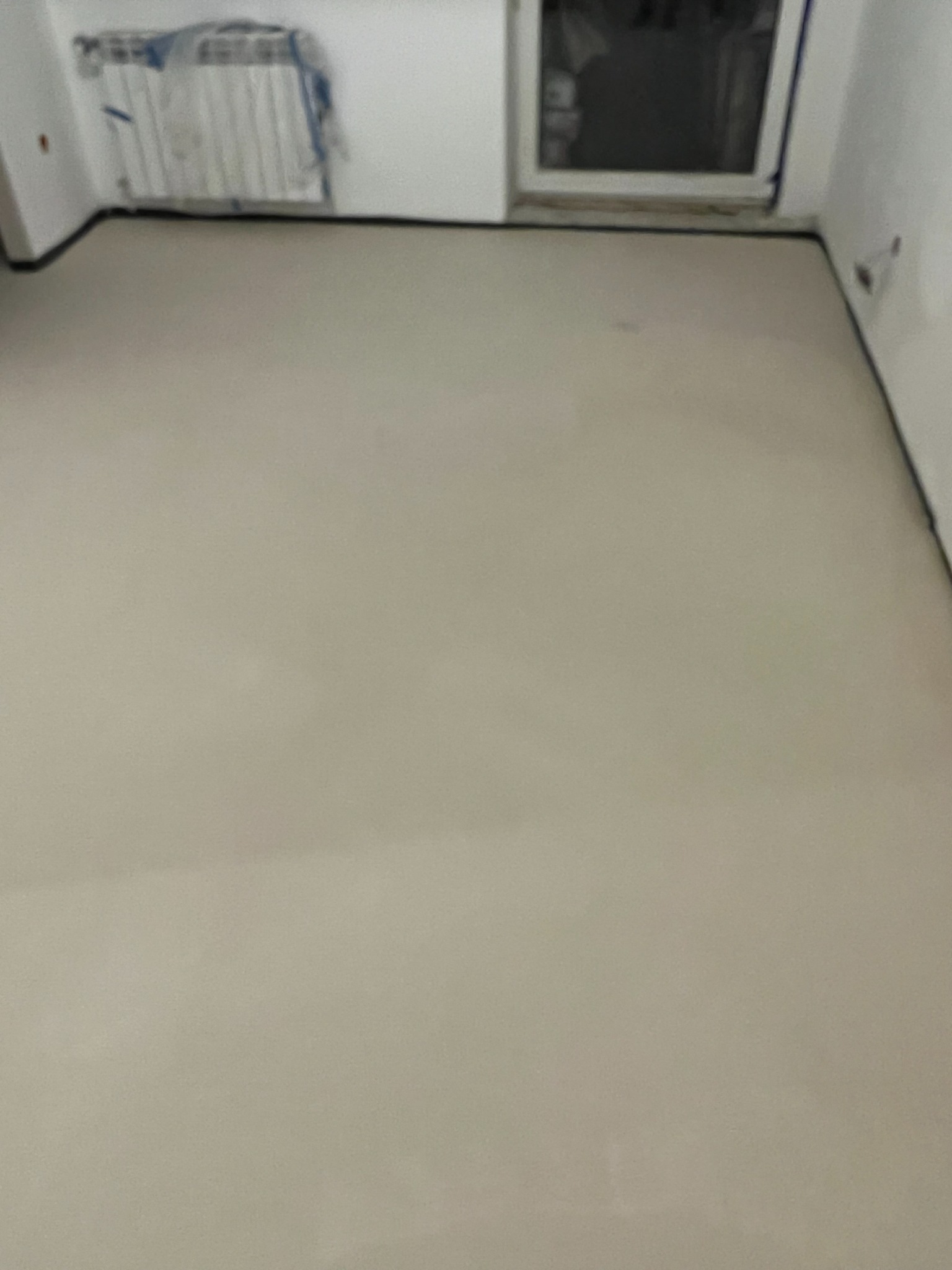 Jasnoszara, gładka wylewka podłogowa w nowym pomieszczeniu z zakrytymi grzejnikami i oknem.