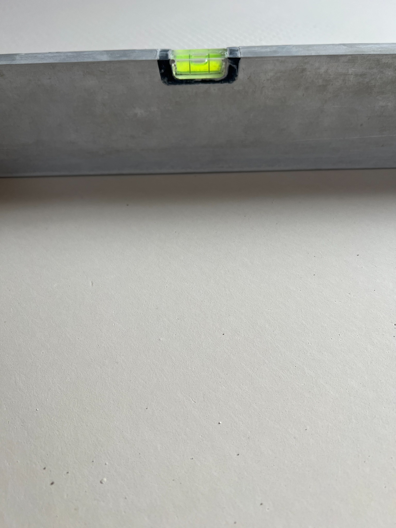 Poziomica na świeżo wylanej, jasnej powierzchni, prawdopodobnie posadzce.