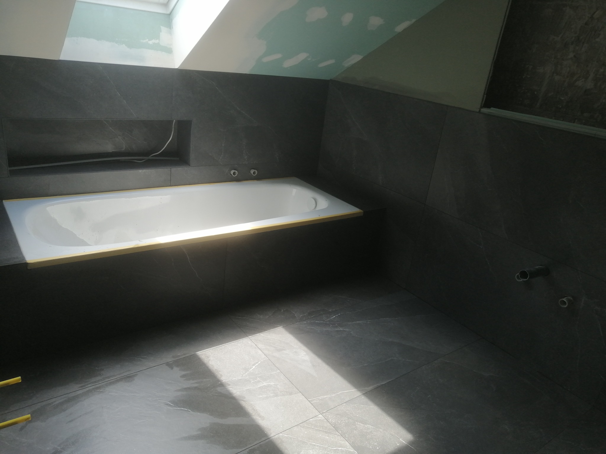 Ciemnoszara łazienka w trakcie wykańczania z wanną, wnęką w ścianie i niedokończonym sufitem na poddaszu.