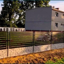 Nowoczesne ogrodzenie panelowe z podmurówką imitującą kamień, widok na dwukondygnacyjny dom w tle.