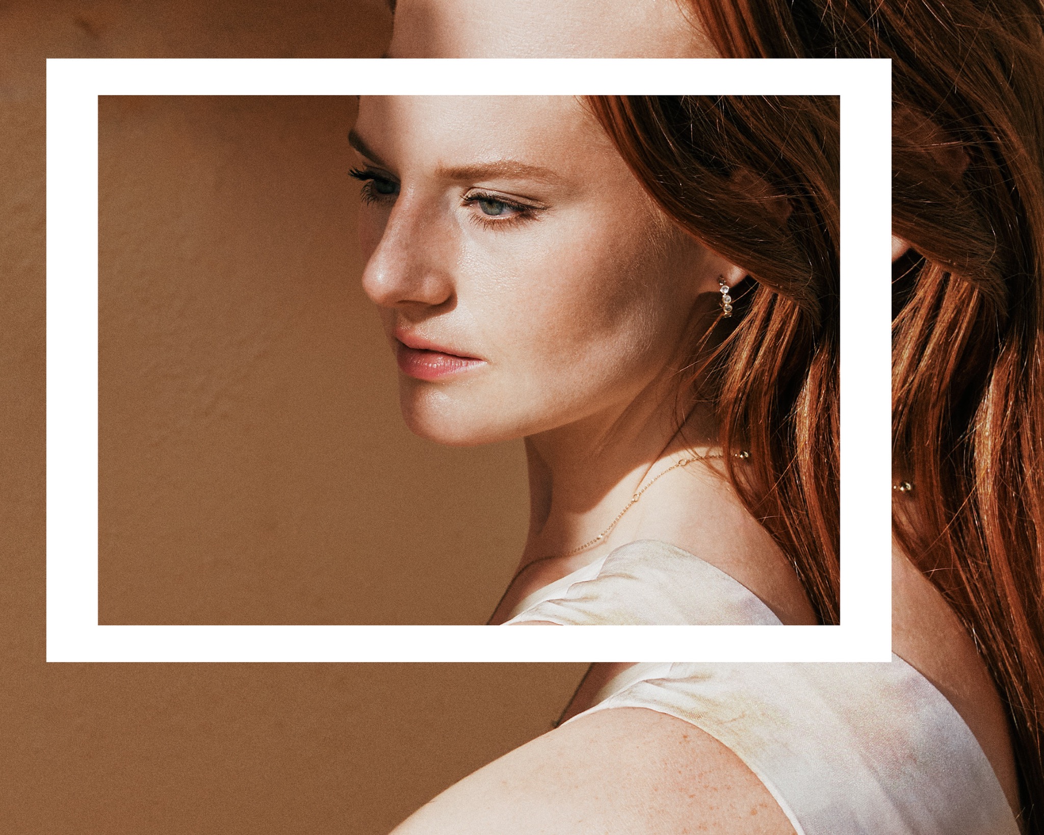 Portret kobiety z rudymi włosami, profil, delikatny makijaż, złota biżuteria, ujęcie w ciepłych tonach, z białym obramowaniem.