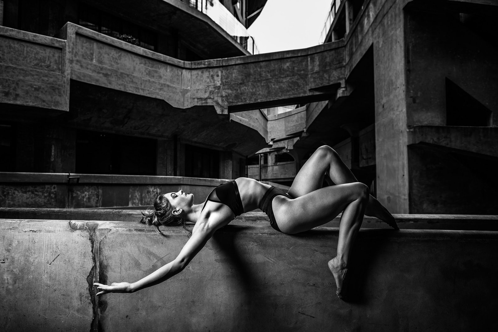 Czarno-białe zdjęcie tancerki baletowej Aneliese Ryan w dynamicznej pozie na betonowej konstrukcji starej rzeźni 1933 Shanghai, Chiny. Unikalna architektura budynku z lat 30. tworzy surowe tło.
