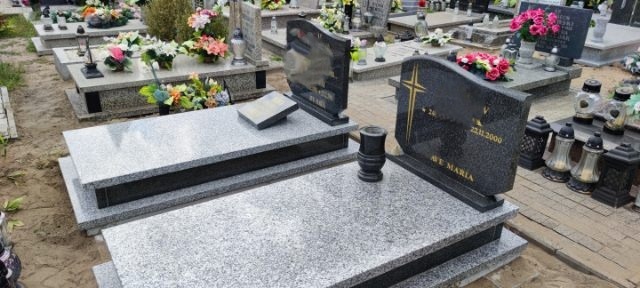 Dwa granitowe pomniki na cmentarzu, jeden z czarnego granitu z wyrytym krzyżem i napisem 'Ave Maria', drugi szary z książką z kamienia.