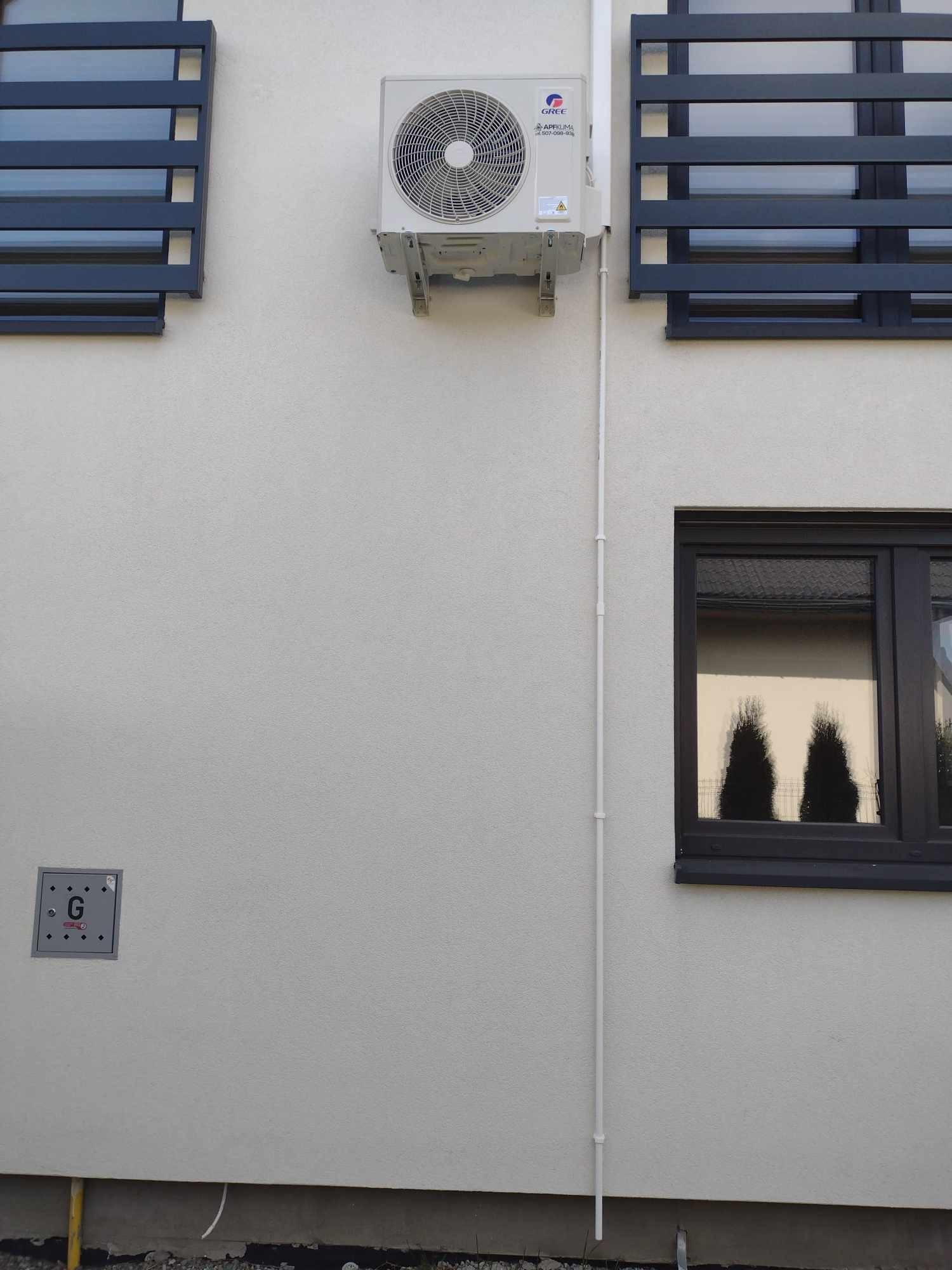 Zewnętrzna jednostka klimatyzacji zamontowana na elewacji budynku z widocznymi oknami i elementami instalacji.