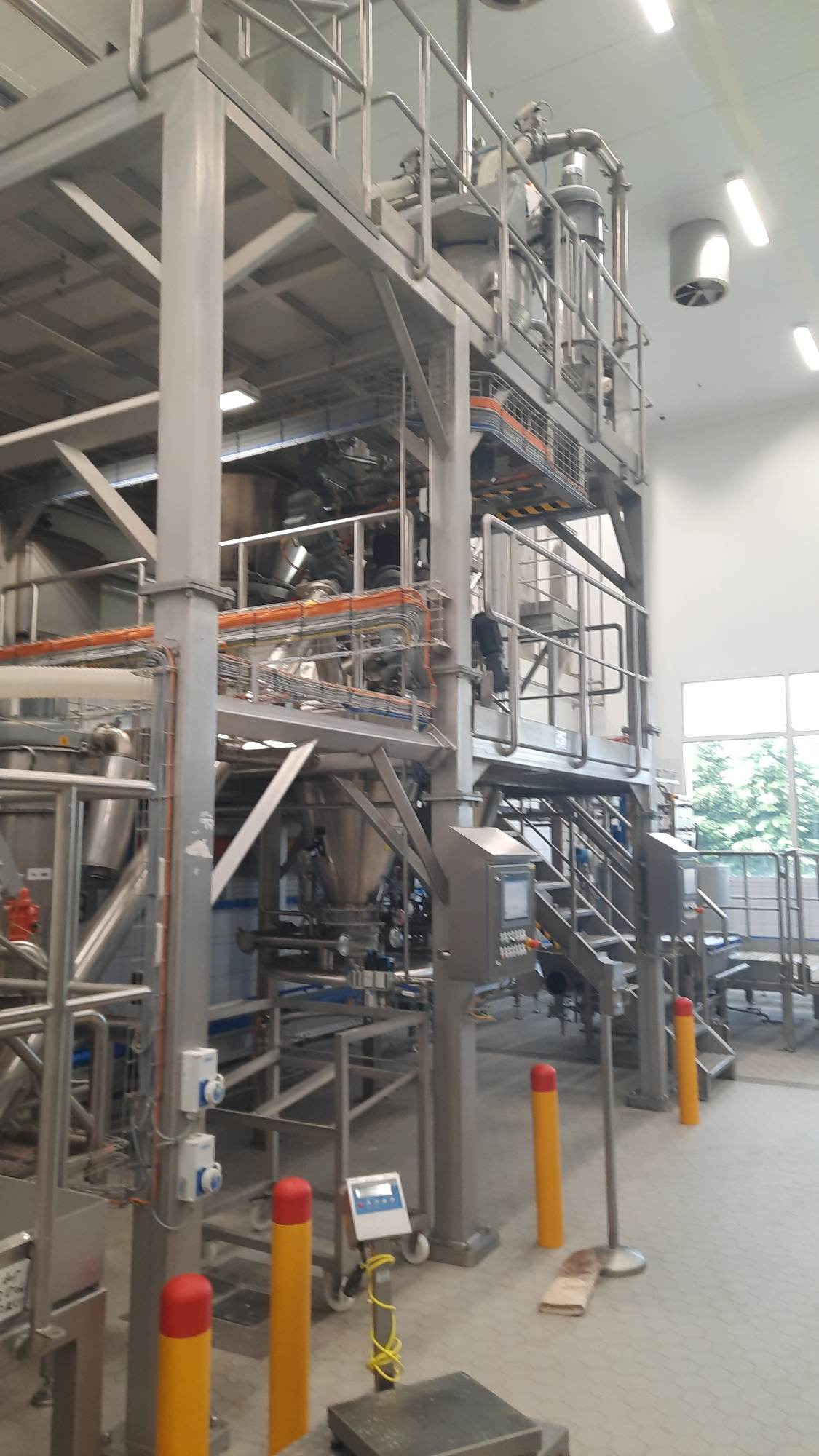 Wysoka stalowa konstrukcja wsporcza z rurami, zbiornikami i schodami w jasnym wnętrzu hali produkcyjnej, z widocznymi elementami sterującymi i zabezpieczeniami.