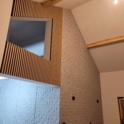 ROSTYSLAV Trokhymenko - Nowoczesne wykończenie wnętrza z drewnianymi lamelami wokół okna i trójwymiarową szarą okładziną ścienną, widoczne drewniane belki stropowe i wiszące żarówki