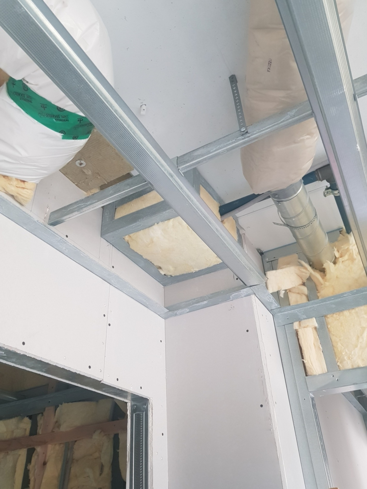 Sufit podwieszany w trakcie montażu: widoczne metalowe profile, płyty gipsowo-kartonowe częściowo zamontowane oraz warstwa izolacji z wełny mineralnej, a także elementy instalacji wentylacyjnej.