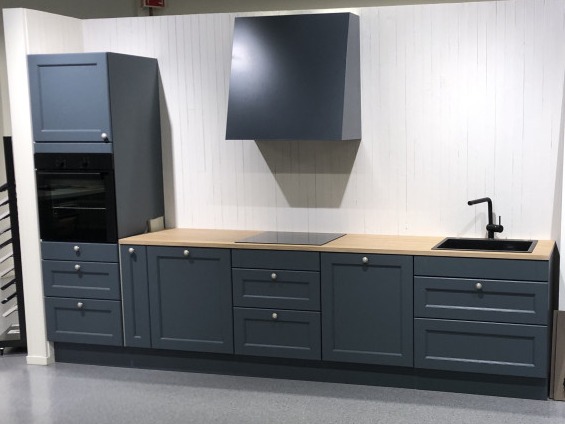 Nowoczesna zabudowa kuchenna w odcieniach szarości z drewnianym blatem, czarną armaturą i płytą indukcyjną na tle białej ściany z pionowymi panelami.