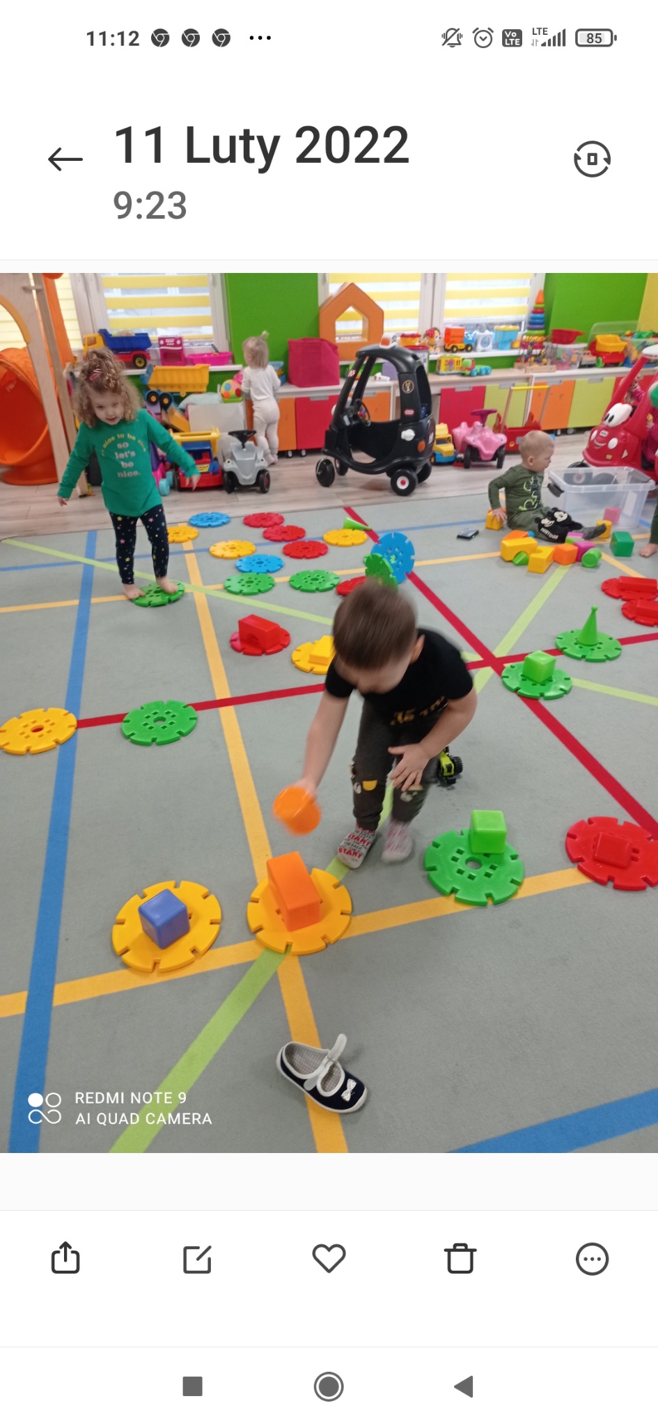 Dzieci bawią się klockami w sali zabaw z kolorowym dywanem i zabawkami w tle.