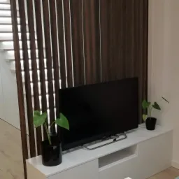 Drewniana ścianka działowa z pionowych listew oddzielająca schody od salonu w mieszkaniu w Krakowie, z telewizorem na białej szafce RTV i stolikiem kawowym.