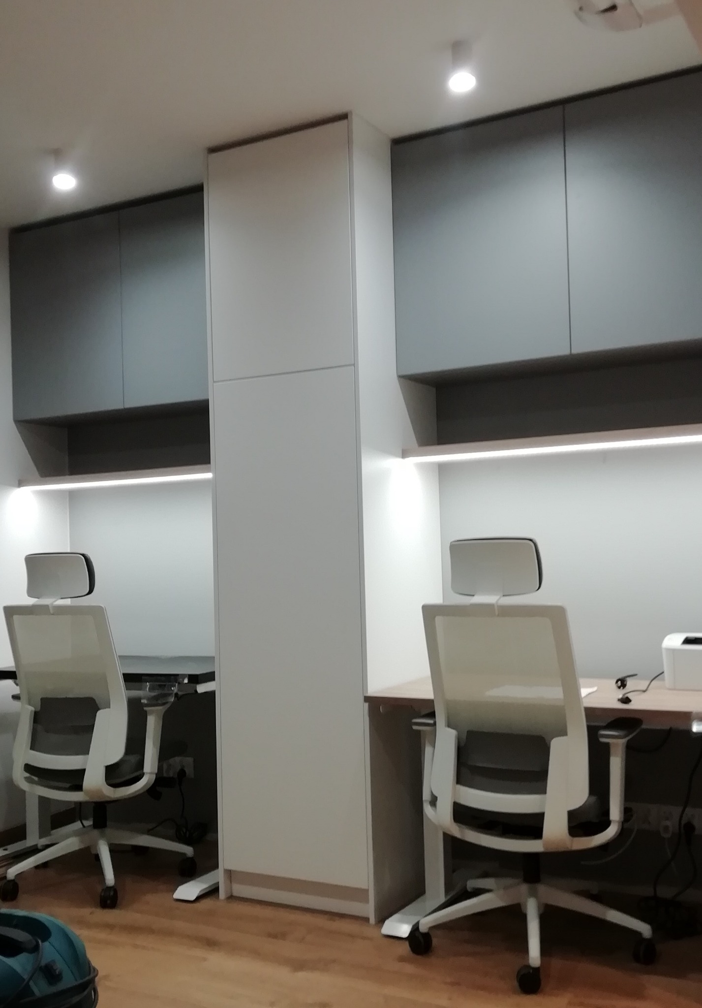 Dwa stanowiska pracy z biurkami i krzesłami, z szafkami wiszącymi i oświetleniem LED, w minimalistycznym stylu.