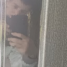 Kamil Sap Schildersbedrijf - Zamazane odbicie osoby w szybie drzwi, widoczne dłonie i fragment twarzy, szare ramy drzwi.