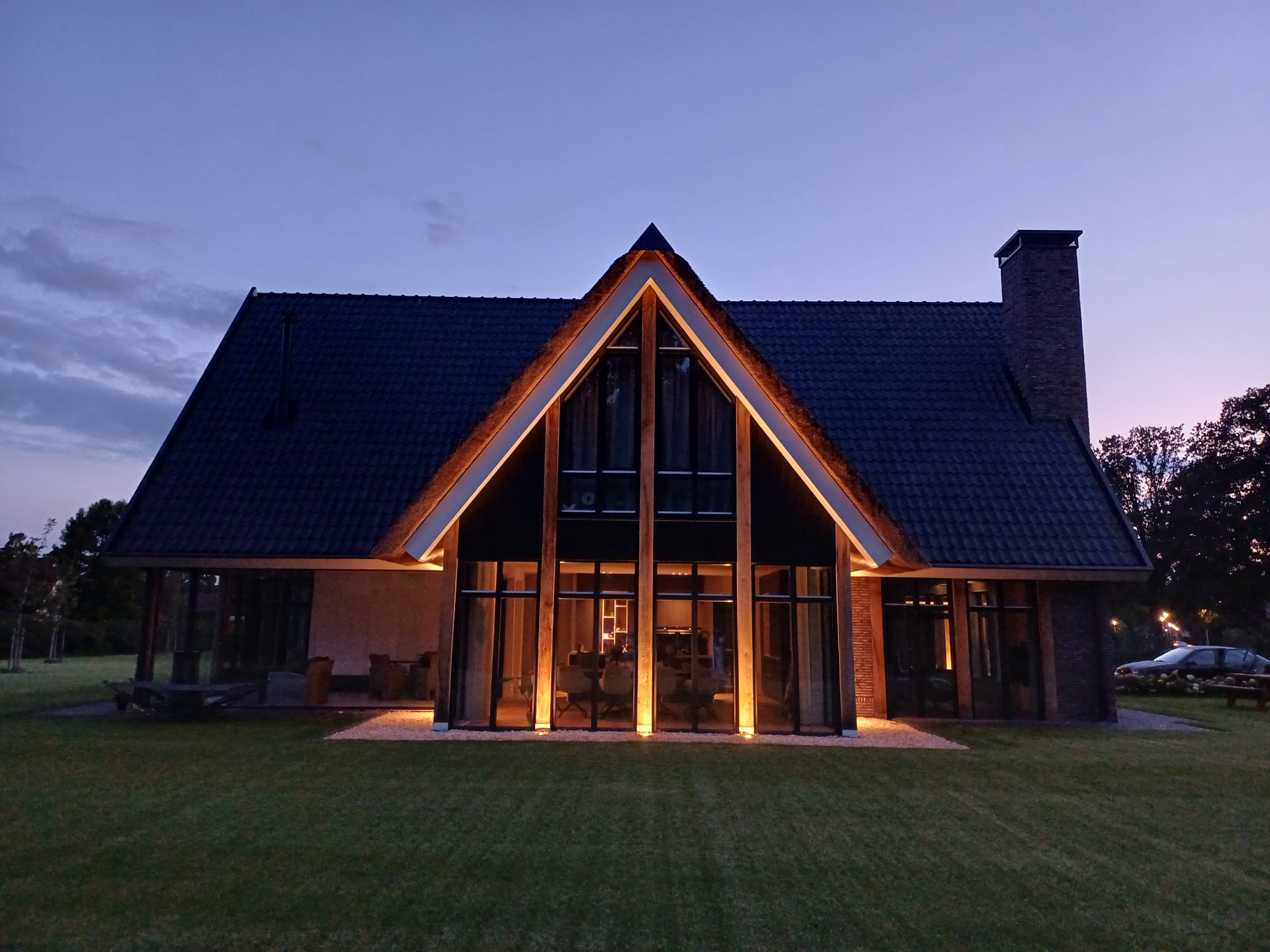 Nowoczesny dom jednorodzinny z dużymi przeszkleniami, oświetlony ciepłym światłem o zmierzchu, widok z zadbanego trawnika.