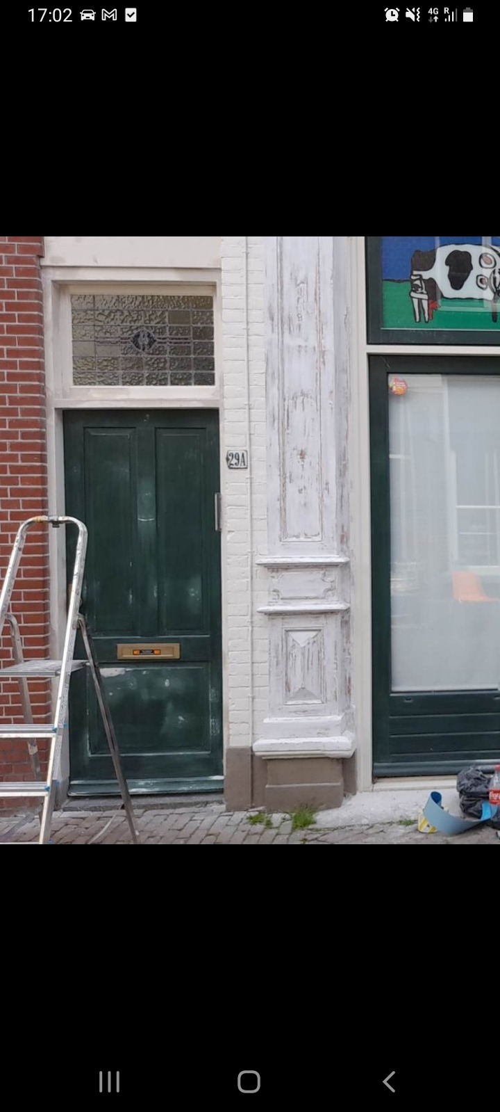 Zielone, dwuskrzydłowe drzwi wejściowe z numerem 29A, widoczne z bliska podczas renowacji elewacji w Gowarczowie, obok drabina malarska i ślady farby na kolumnie.