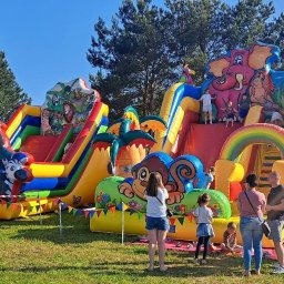 BAWEO BARBARA WÓJCIK - Kolorowe dmuchańce z motywem dżungli i Paw Patrol na zielonej trawie, otoczone grupą ludzi w słoneczny dzień. Widoczne drzewa w tle.