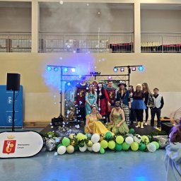 BAWEO BARBARA WÓJCIK - Scena z grupą osób w kostiumach, oświetlona reflektorami i otoczona dekoracjami z balonów i banerem Warszawa Ursus. Efekty specjalne w postaci baniek mydlanych.